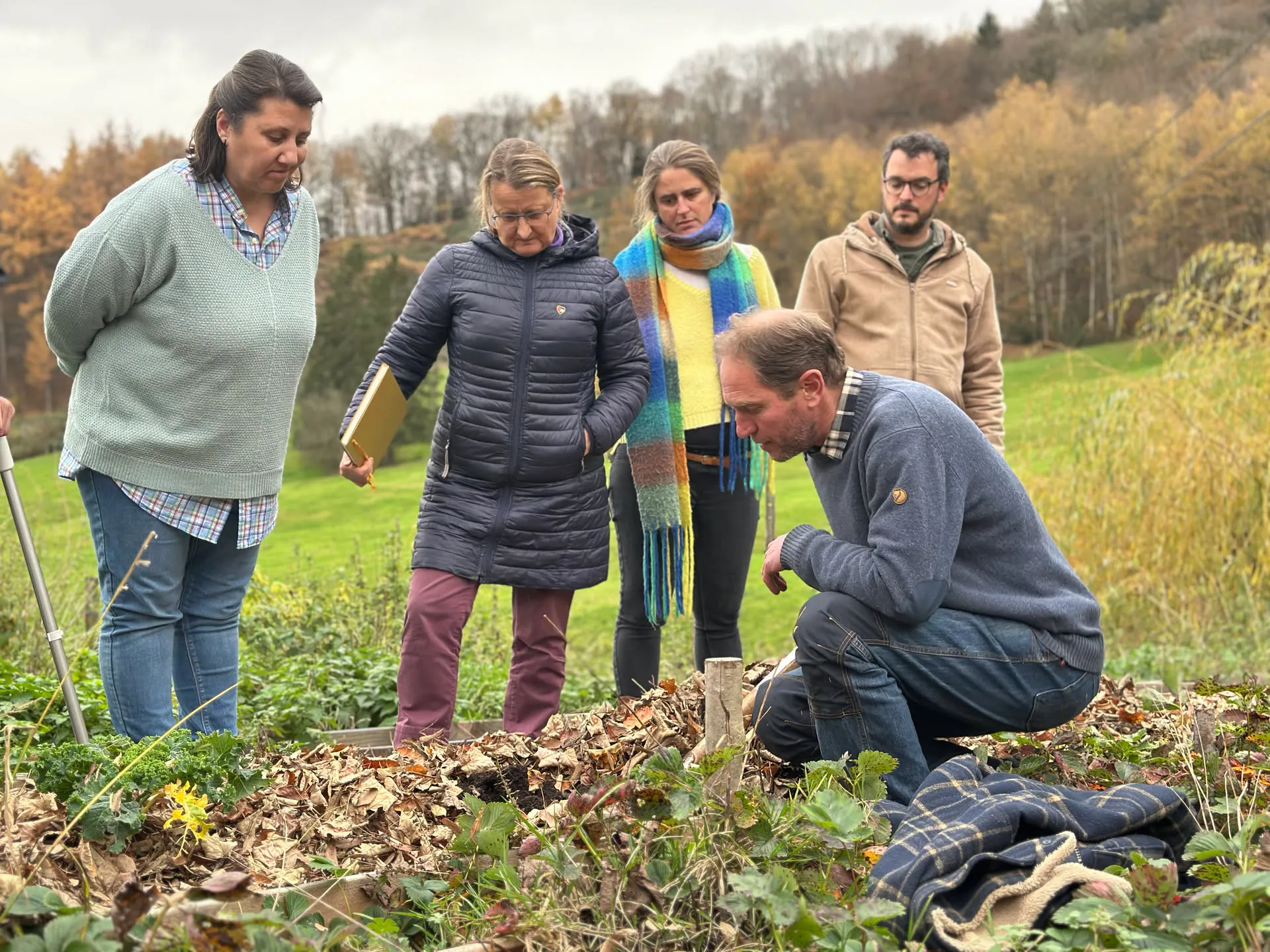Un petit groupe rassemblé autour d’une planche de culture paillée de feuilles mortes, en pleine discussion, dans un paysage aux couleurs d’automne