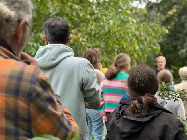 Participant·es rassemblé·es autour d'un formateur dans un jardin-forêt
