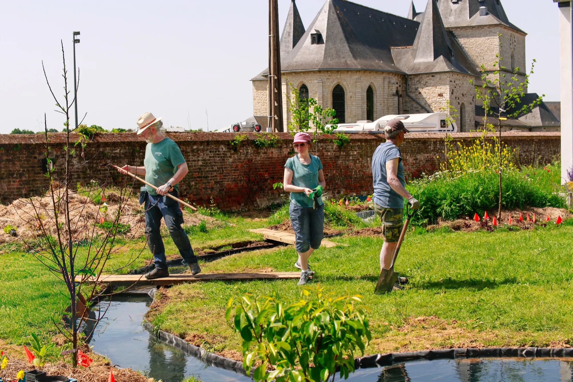 Chantier bénévole dans un jardin nourricier clos de murs, une église en arrière-plan